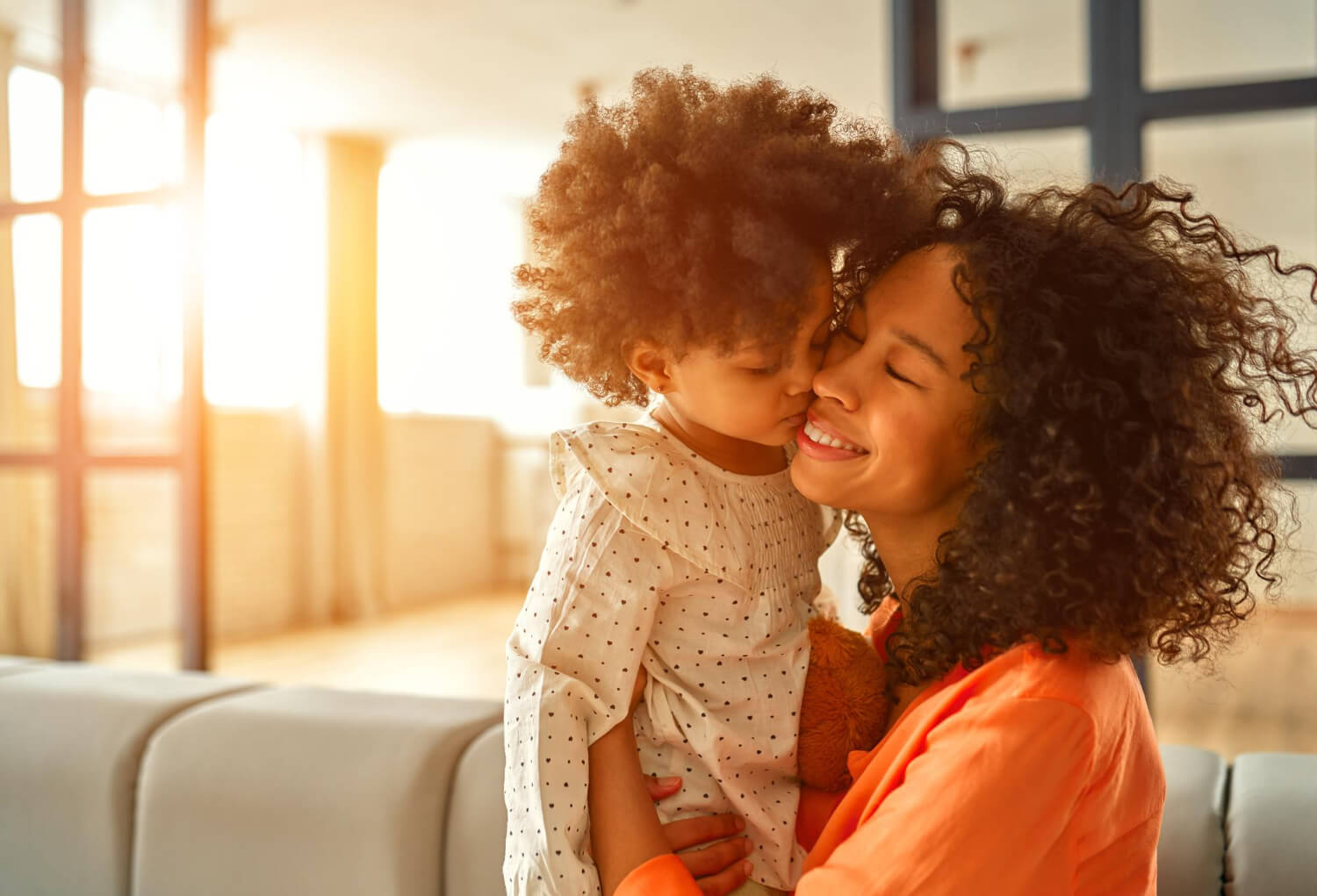 african-american-woman-wither-little-daughter-with-curly-fluffy-hair-sitting-sofa-gently-hugging-living-room-home-1